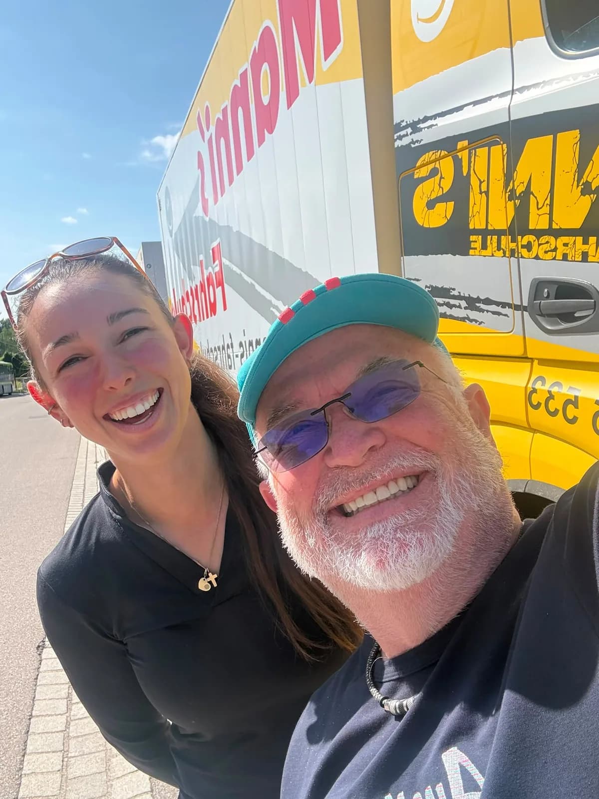 Manni und eine Fahrschülerin lachen vor dem gelben Schulungs-LKW