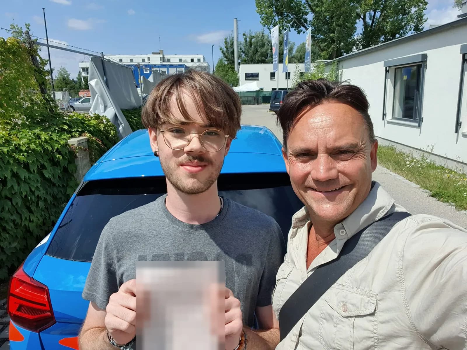 Fahrschüler und Fahrlehrer vor dem blauen Fahrschulauto nach der bestandenen Prüfung